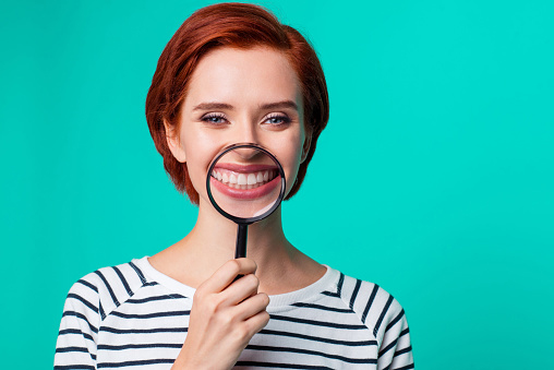  Woman holding magnifying glass over her teeth
