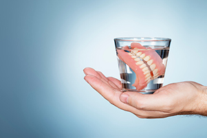  hand holding a glass with a full set of dentures in it