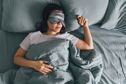 Top-down view of a woman sleeping in bed while wearing a sleeping mask