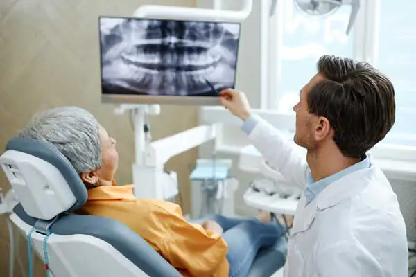 Back view of male dentist pointing at tooth X-ray image on screen during consultation at Cooley Smiles in Everett, WA