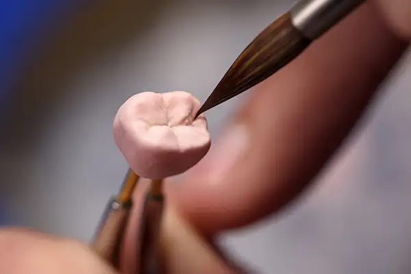 Close-up of a dental technician sculpting the final details on a dental crown using precise tools.