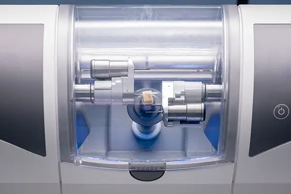 A CAD/CAM dental milling machine crafting a dental crown from a ceramic block in a dental lab.