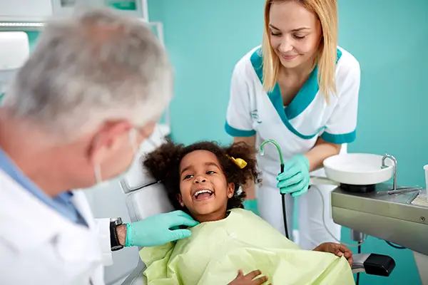 Adorable and young Black girl sitting in a dental chair and smiling at her dentist and assistant at Hoffman Dental in Hillsboro, OR