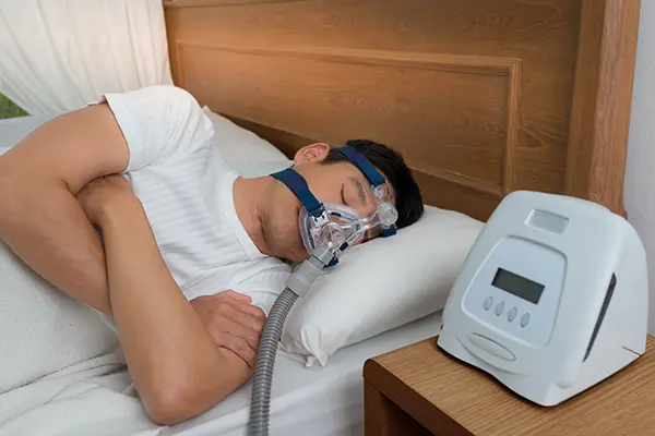 Man resting comfortably in bed with a CPAP sleep apnea machine strapped over his mouth and nose by Cooley Smiles in Everett, WA
