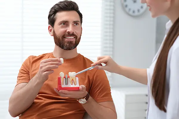 A patient holds a model of teeth with a single dental implant, while discussing benefits of mini dental implants with his dentist.
