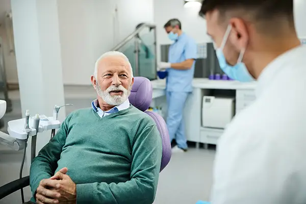 An older male patient sitting in a dental chair and consulting with a dentist about dental implants at Hoffman Dental in Hillsboro, OR An older male patient sitting in a dental chair and consulting with a dentist about dental implants at Hoffman Dental in Hillsboro, OR