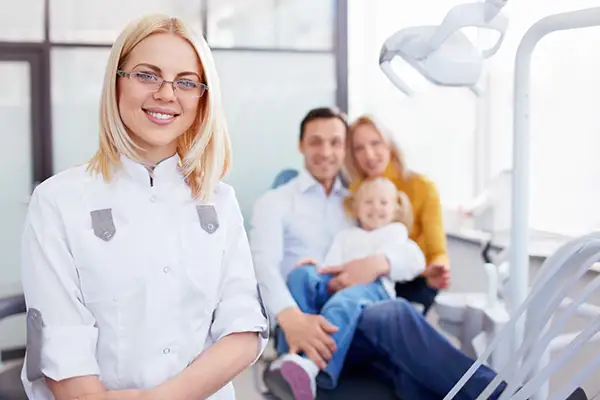 A female dentist smiling and standing in front of a family sitting in the dentist chair at Hoffman Dental in Hillsboro, OR