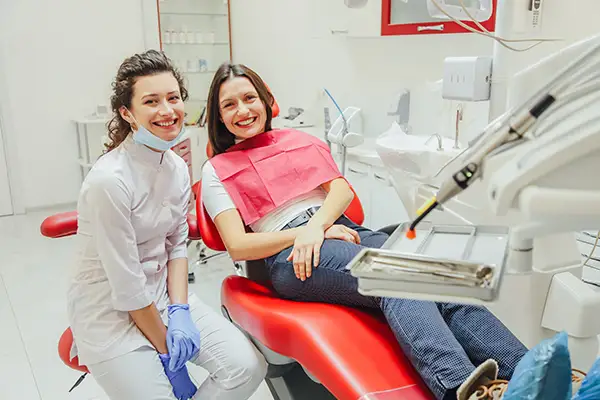 A dentist smiling brightly with her seated patient, explaining tooth replacement options at at Hoffman Dental in Hillsboro, OR