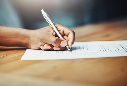 Hand filling out a new patient form with a pen