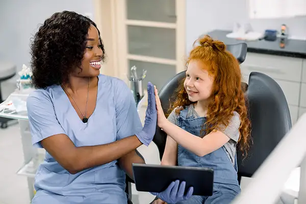 A smiling young girl and her dentist high-fiving each other after cavity treatment at Hoffman Dental in Hillsboro, OR