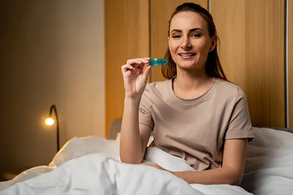 Woman sitting in bed holding a blue night guard from Hoffman Dental in Hillsboro, OR