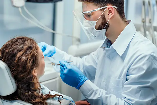 Male dentist wearing protective gear conducting an oral check up on a female patient at Jillian Prather Family Dentistry in Owasso, OK